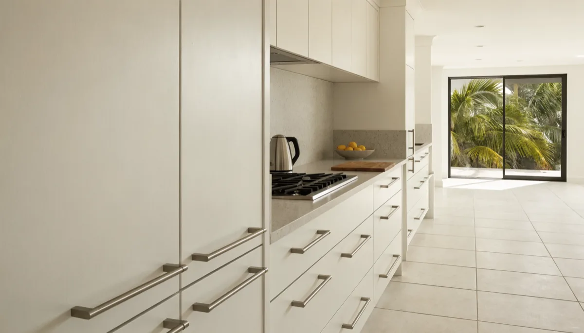 Accessible kitchen remodeling Davie, FL: a finished kitchen with a wide clear floor running the length of the room, warm white slab drawers under a pale gray quartz counter and a full height stone backsplash