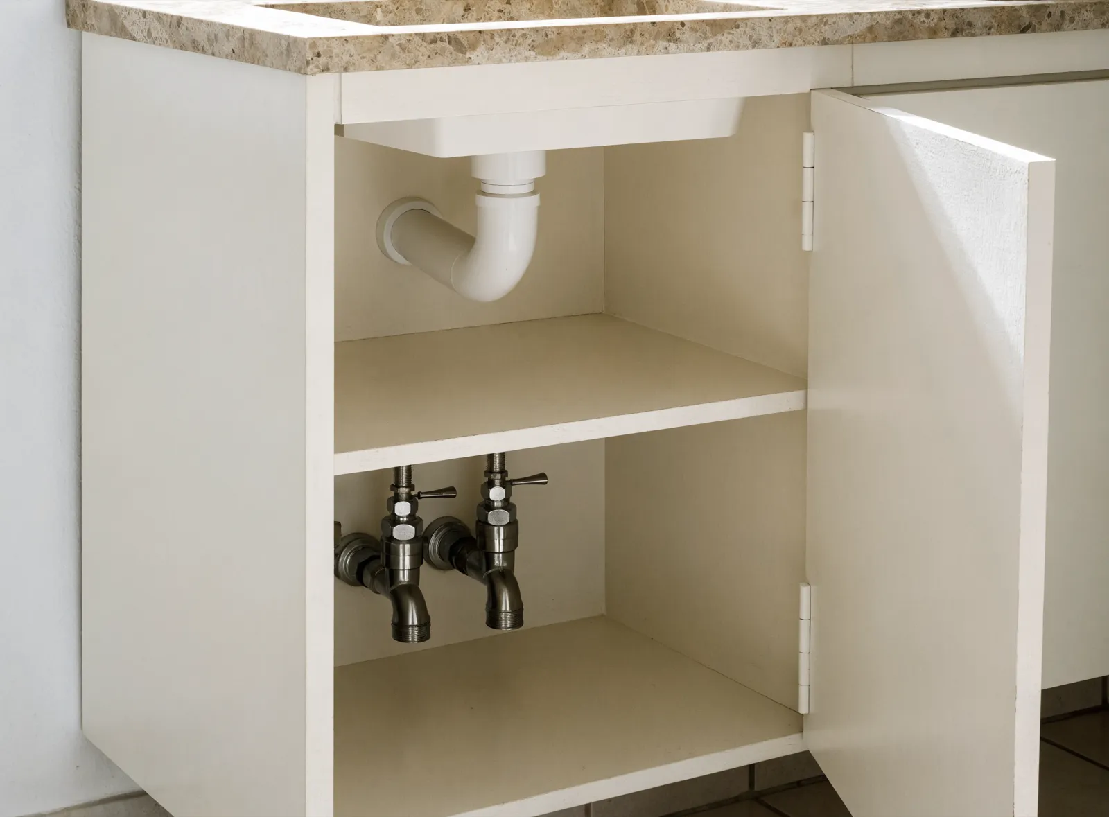 A bathroom vanity in Davie, FL with one door open, the drain trap and the two shutoff valves visible inside the cabinet