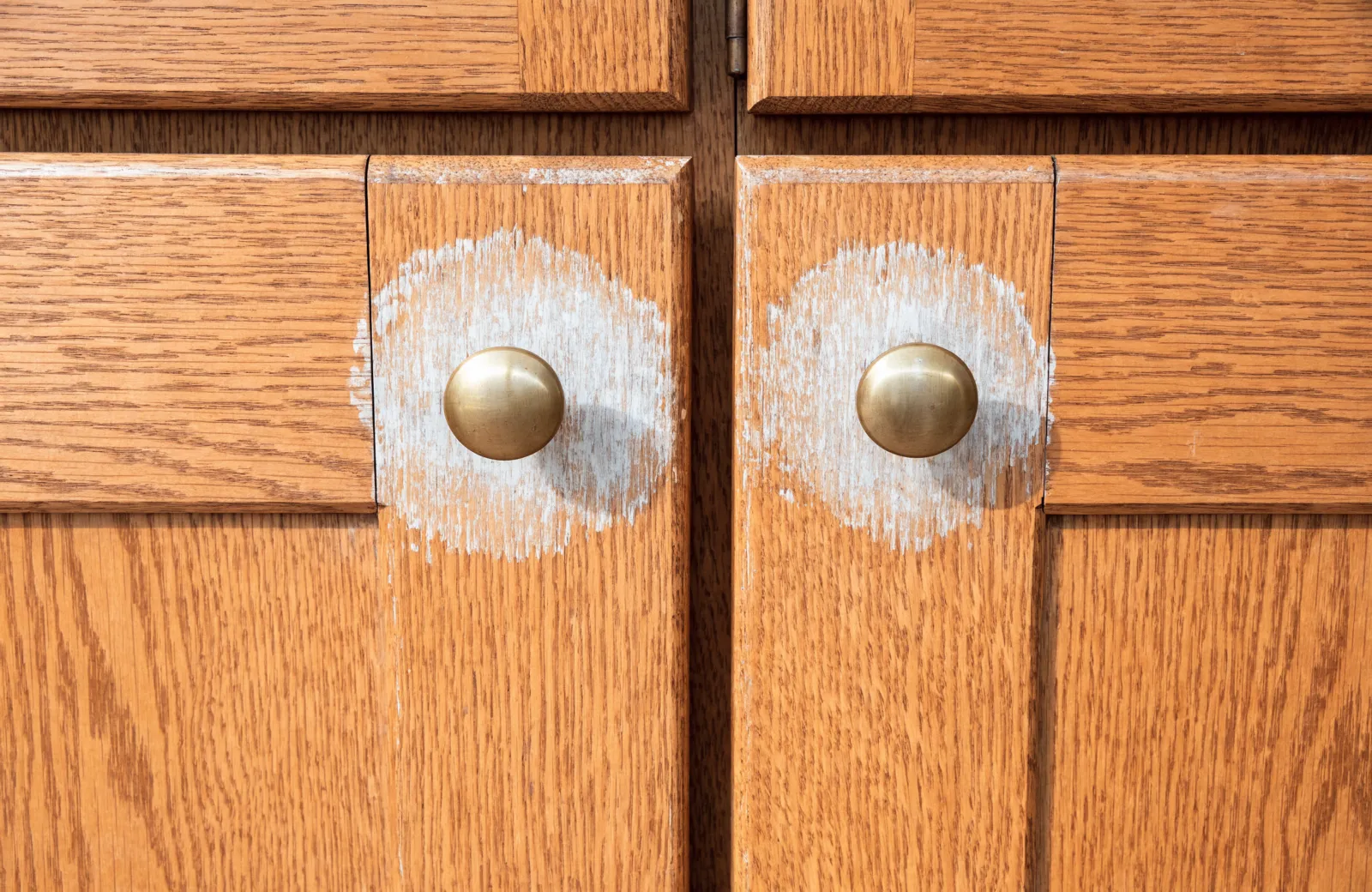 The original brass knobs on an oak wall cabinet in a 1980s Davie kitchen, the finish worn light around each one