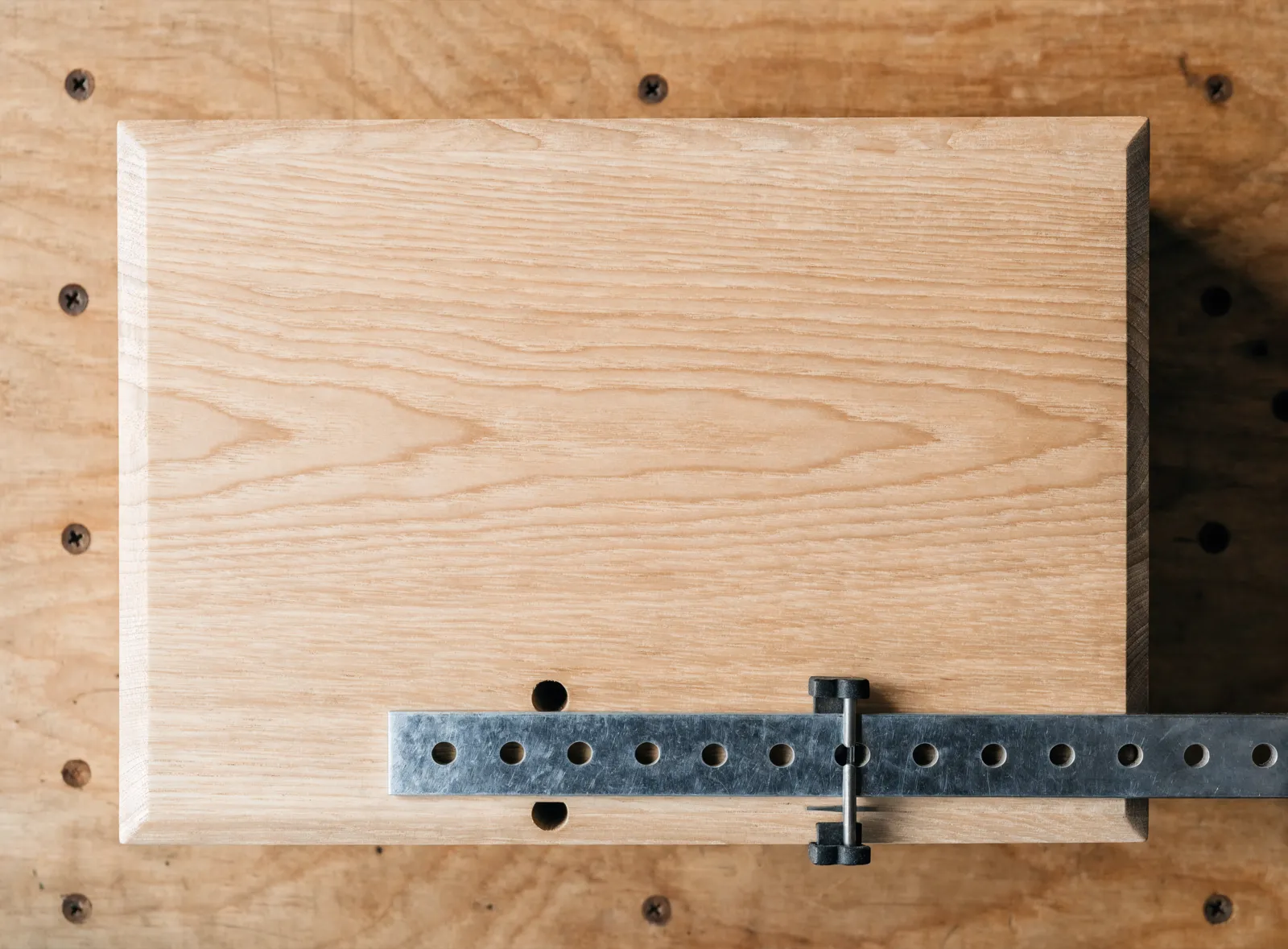 Cabinet hardware installation in Davie, FL: a steel drilling template clamped against the corner of a drawer front, with the two hole positions lined up on it