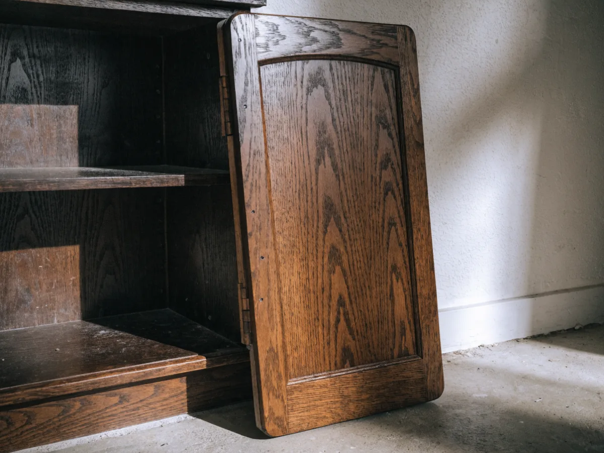 A single dark wood cabinet door leaning against the wall next to the cabinet it came off, the hinge mark still visible on the edge