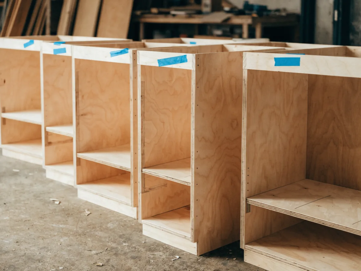 New cabinet boxes assembled and stacked in the shop, the field measurements written on tape across the fronts