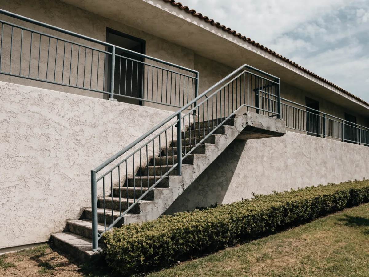 The open exterior stair of a two story condominium in Davie and the landing it reaches, a railed walkway with unit doors opening onto it