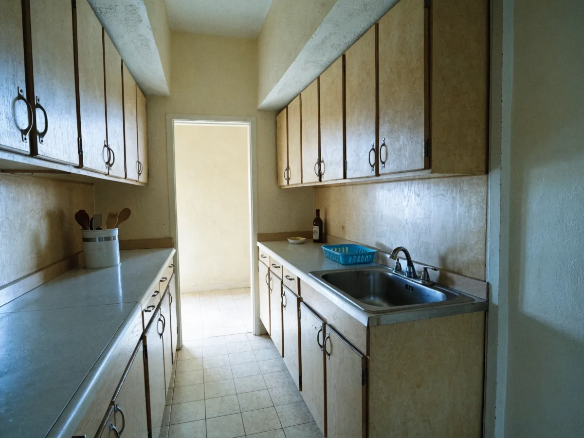 An original 1970s galley kitchen in Davie: melamine cabinets, a closed soffit over the wall units and a filler strip between the run and the wall