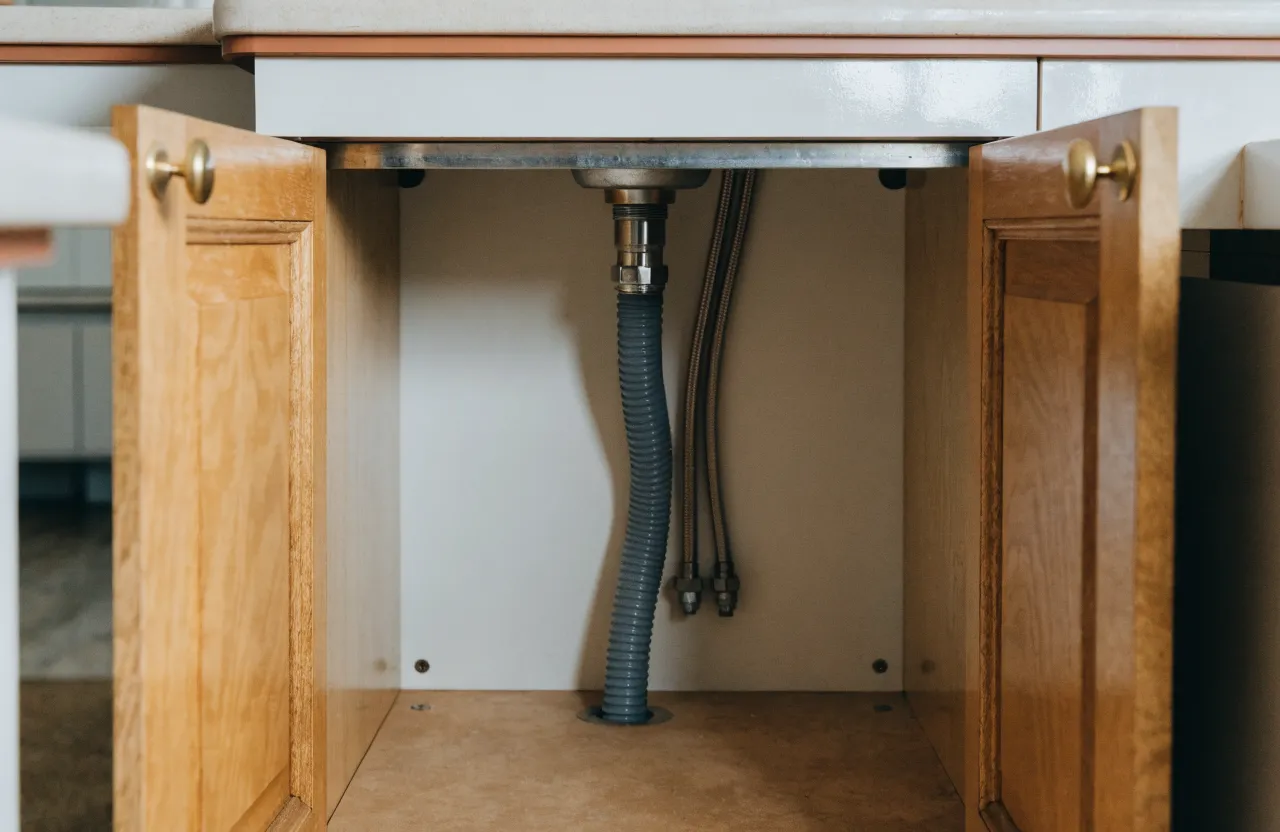 The sink base of that same kitchen with both oak doors swung wide, the floor of the box and its back corners dry and square