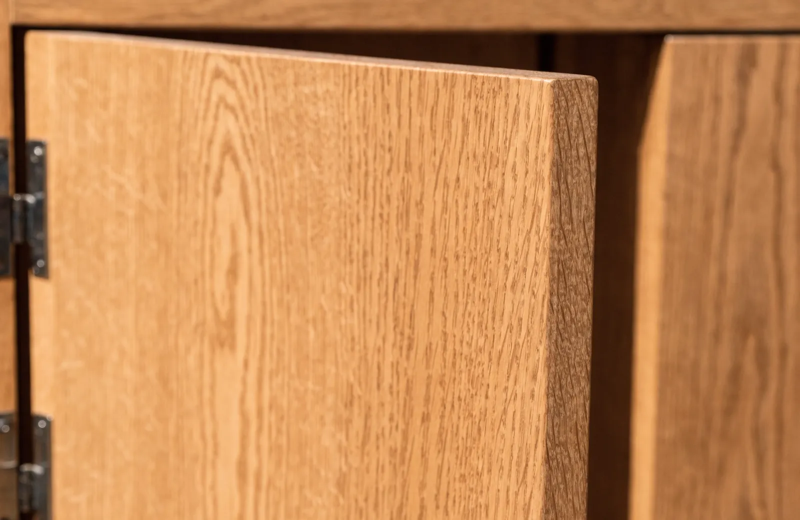 The open edge of a cabinet door seen from the hinge side, grain carrying around the corner and running through the full thickness of the stile