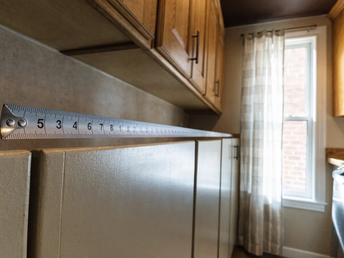 A tape measure extended along the cabinet run against the back wall of a kitchen in old Davie, no people in the frame