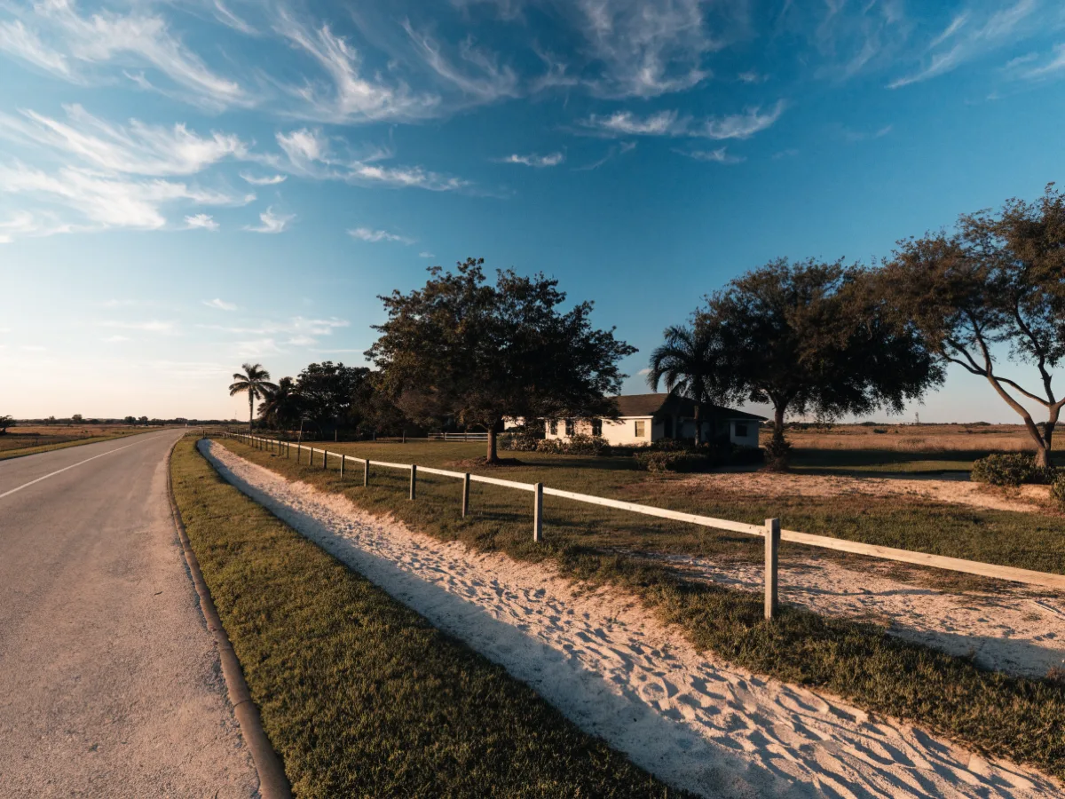 A wide lot frontage on the west side of Davie, one house set well back from the road, a low open fence and a sand trail running outside the fence line in the foreground