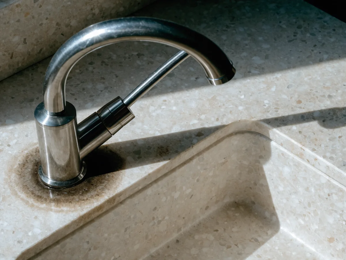 A permanent dark absorption ring in a light stone counter around the faucet base, in a kitchen near Pine Island Ridge in Davie