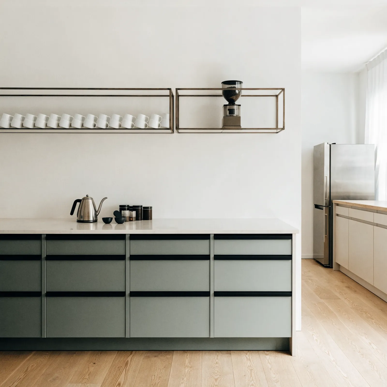 A coffee bar built onto a blank wall beside a Davie kitchen, counter with a drawer bank under it and two shelves above holding mugs and a grinder