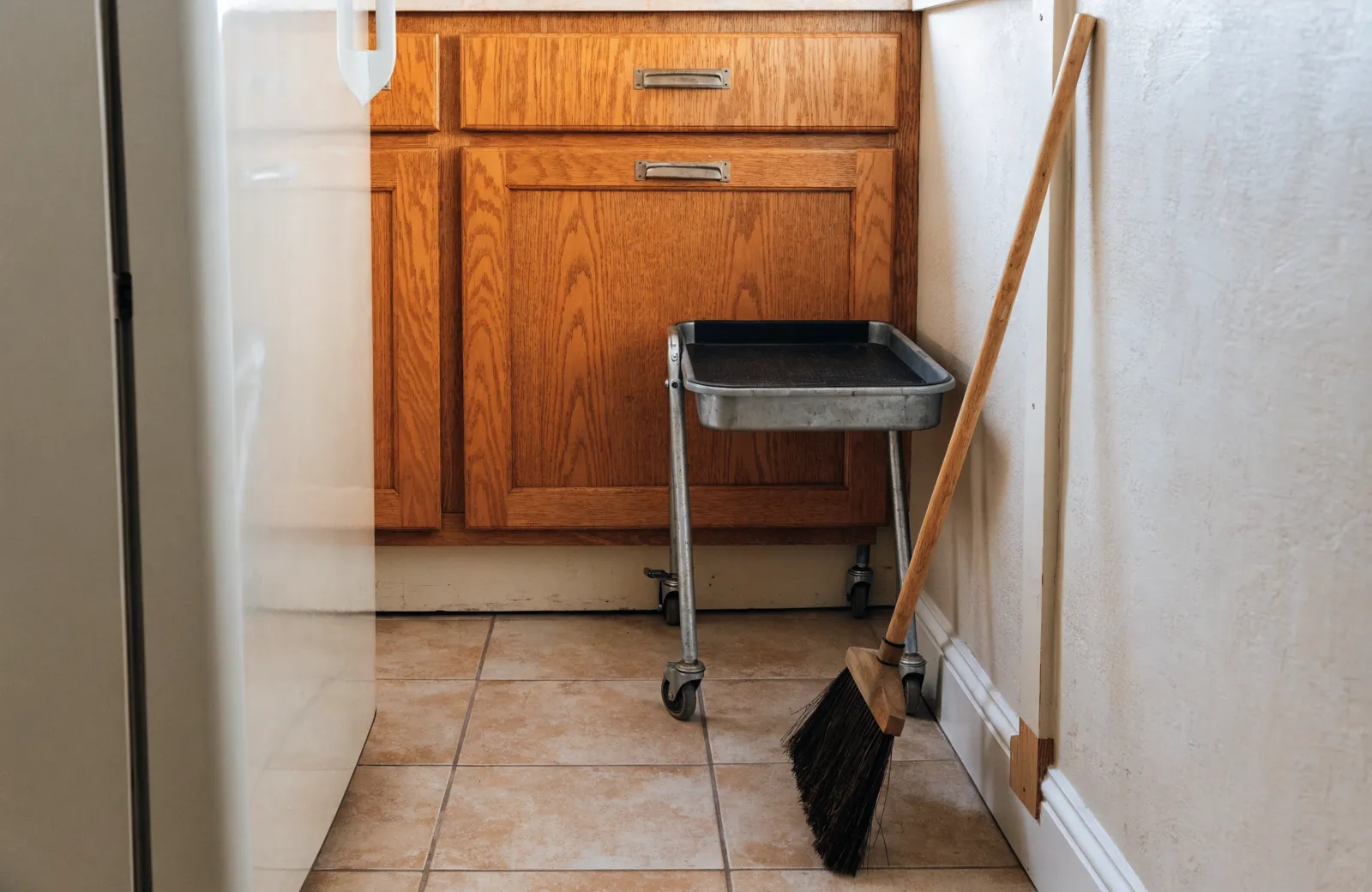 The gap between a refrigerator and the wall in a Davie kitchen, holding a rolling cart and a broom, with the filler strip of the old cabinet run visible
