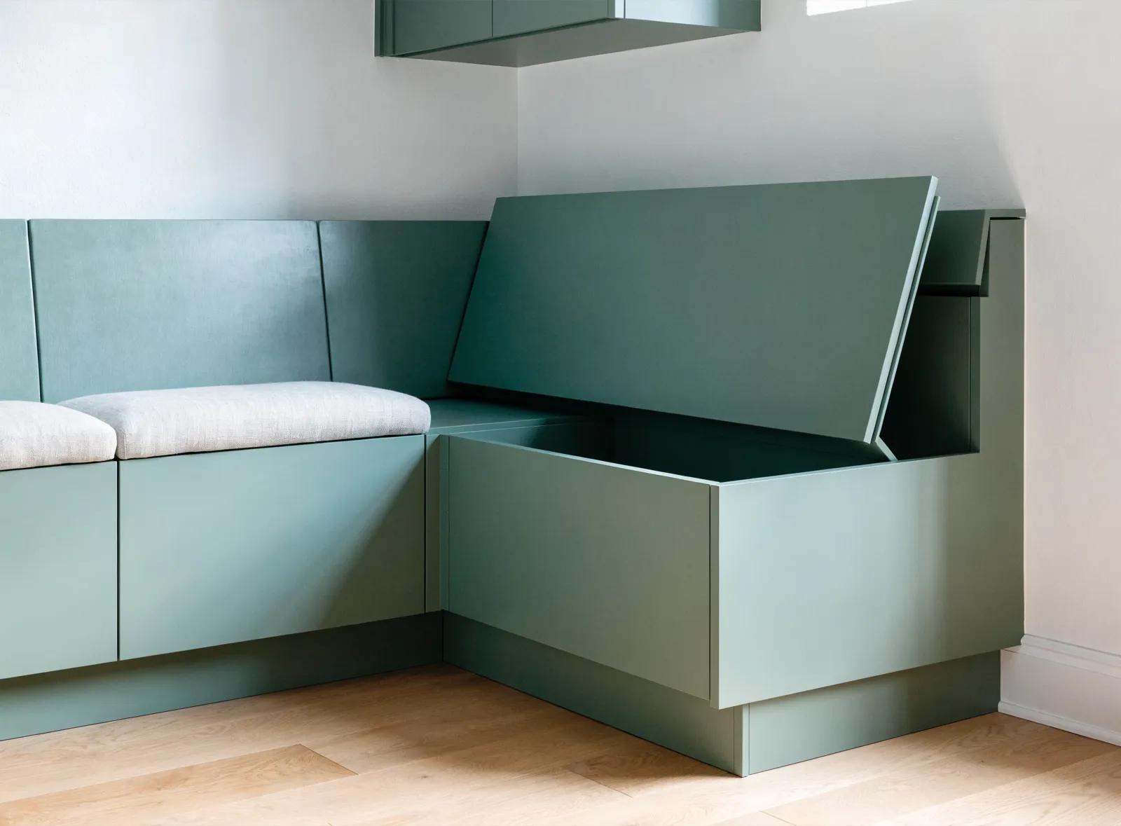 Custom built-ins in Davie, FL: the return of a banquette scribed tight to the wall, the seat lid raised and the storage bay under it open
