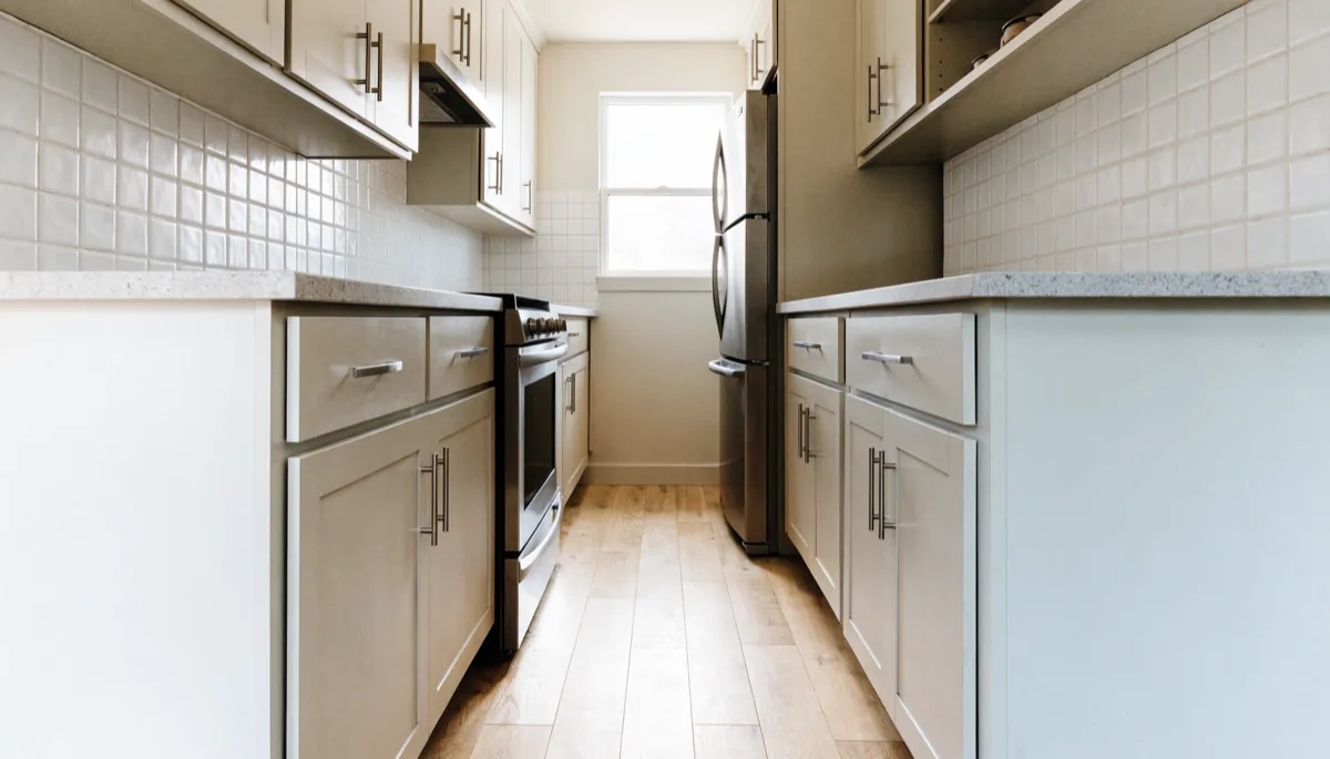 Galley kitchen remodeling Davie, FL: a finished galley kitchen seen along its length, two parallel runs of pale cabinetry with a clear aisle between them and a window at the far end