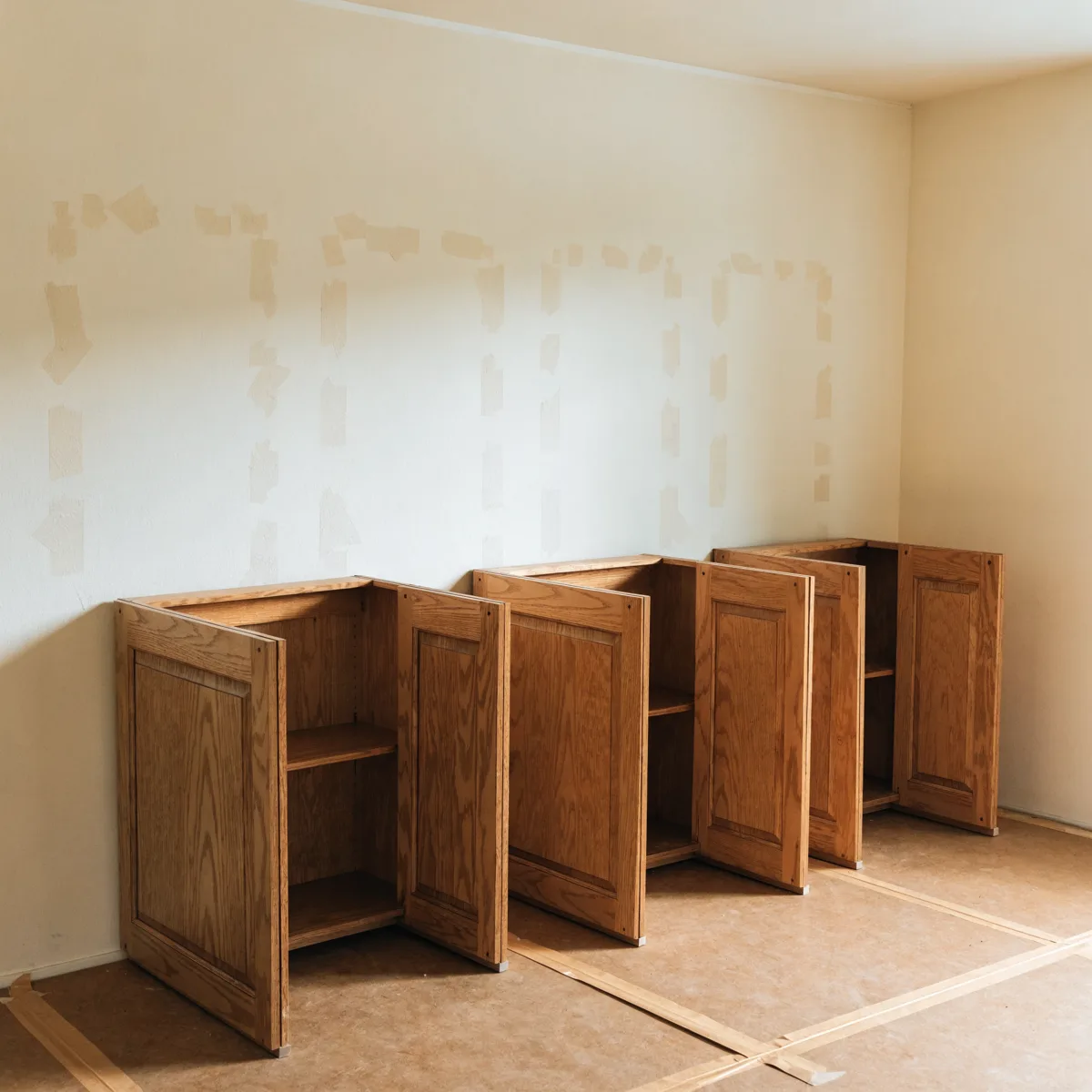 Old honey oak wall cabinets from a Davie kitchen taken down whole and standing in a row against the bare wall, doors closed and undamaged