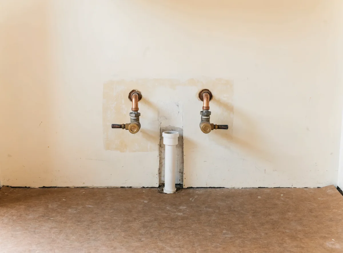 The sink wall of a Davie kitchen after the base cabinets came out, two copper stubs with their lever valves turned off and a capped drain stub against the painted wall