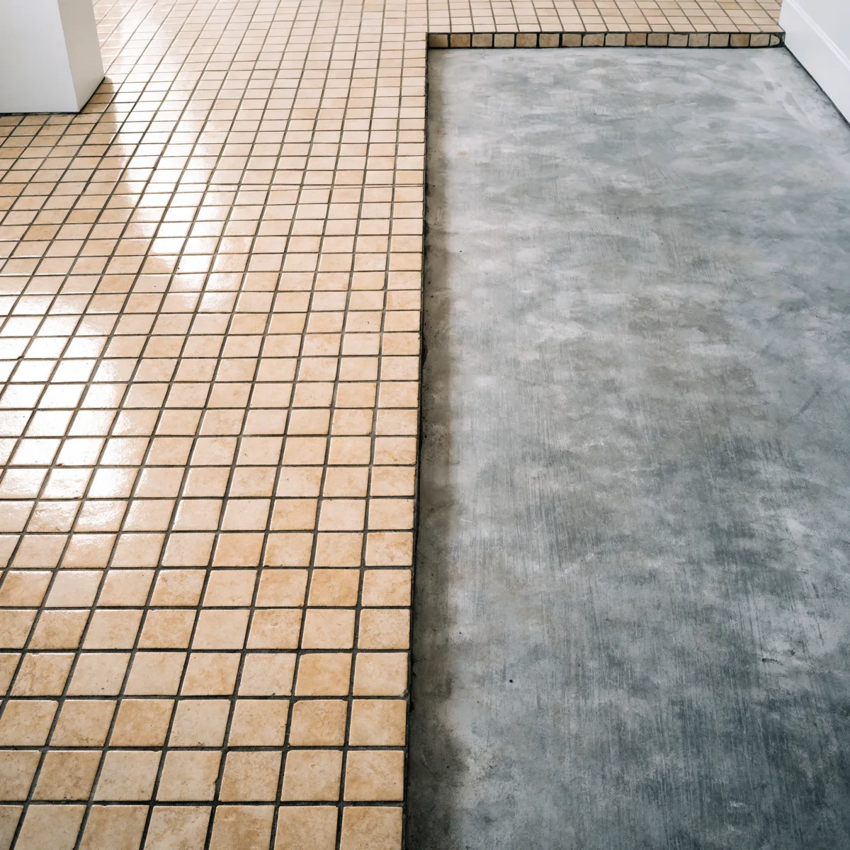 A Davie kitchen floor halfway through removal, old beige tile on one side and clean bare slab on the other with a single straight cut edge between them