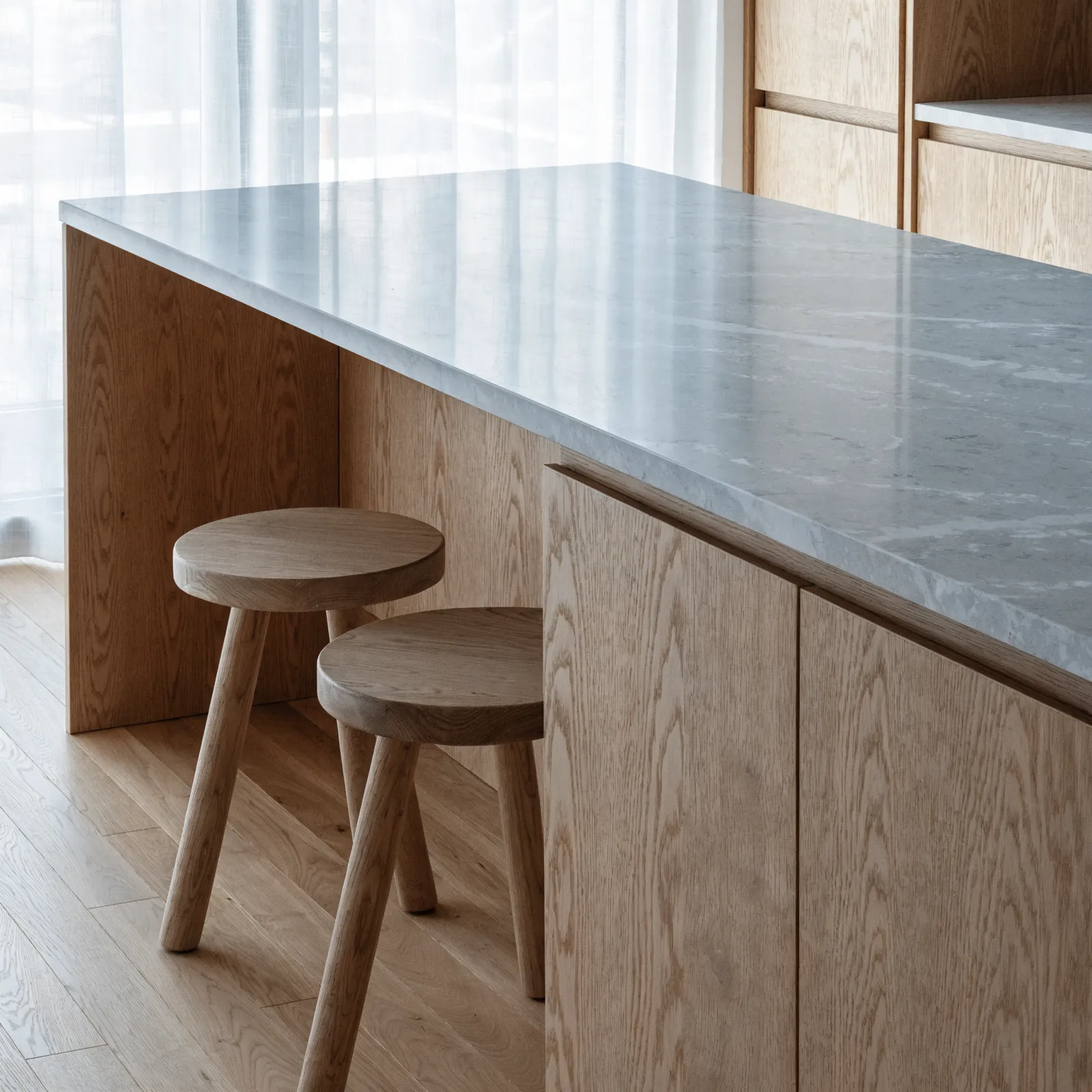 A seating island: the countertop running past the cabinet line to leave knee space, two stools pulled under the overhang and a support panel below