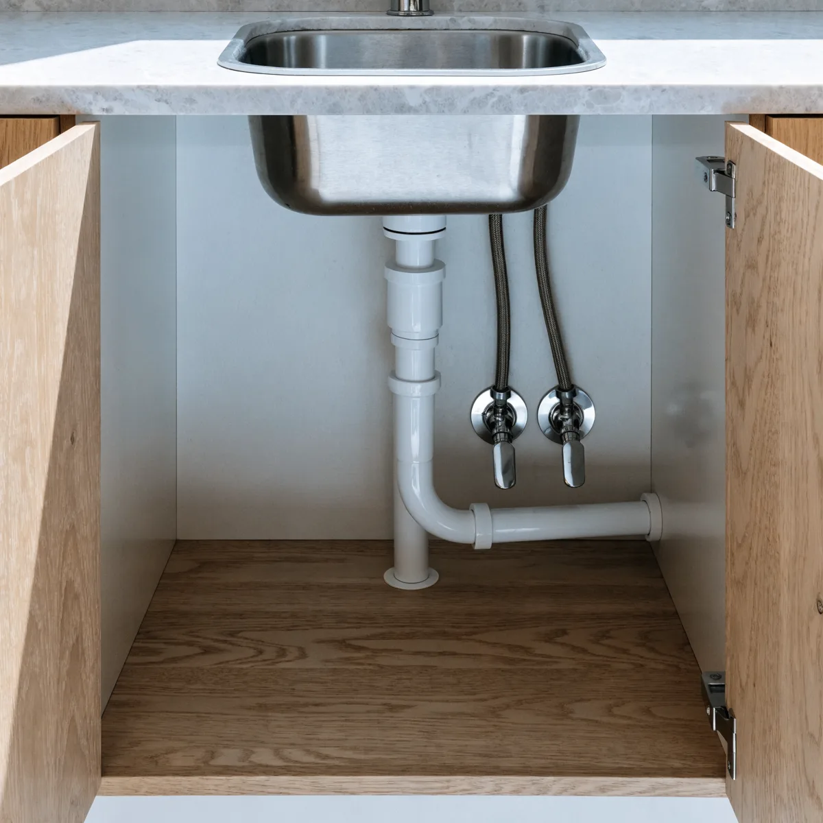 The open base cabinet under a kitchen sink in Davie, FL, with the drain trap and the two supply lines running back into the wall behind them