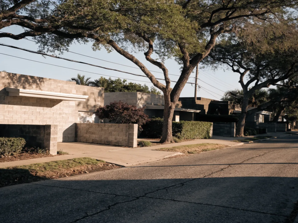 A street of one story block houses in the same part of Davie, private driveways, low front walls and mature laurel oaks over the pavement