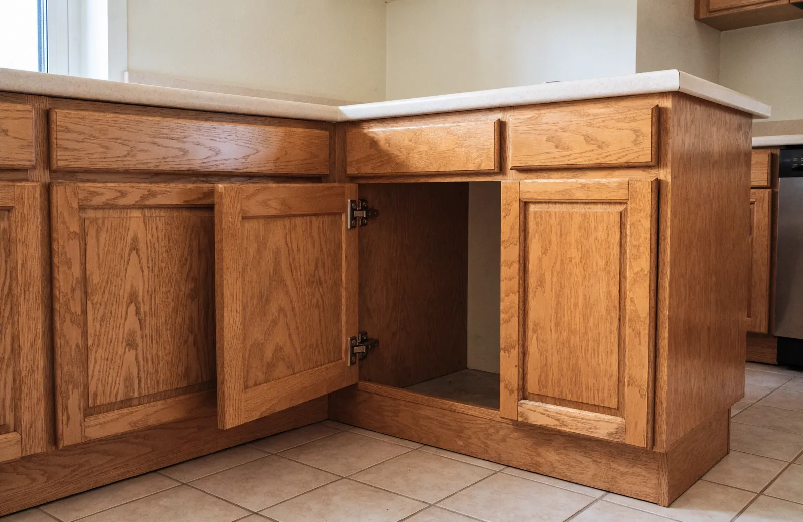 A blind corner base cabinet with its single door open, the cabinet run continuing sideways past the opening into a space with no door of its own