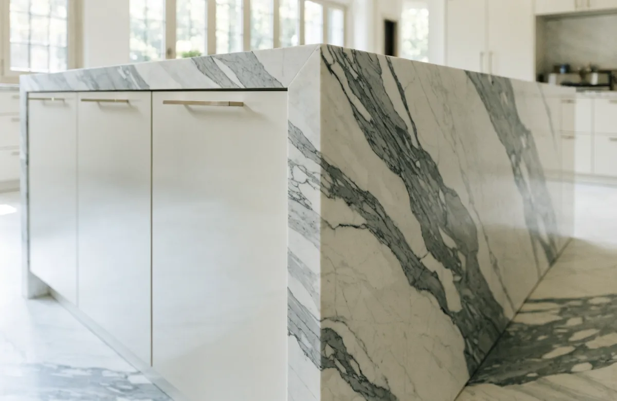 The end of that island from the side, the marble waterfall running to the floor beside the lacquered doors and the veining carried around the mitered corner