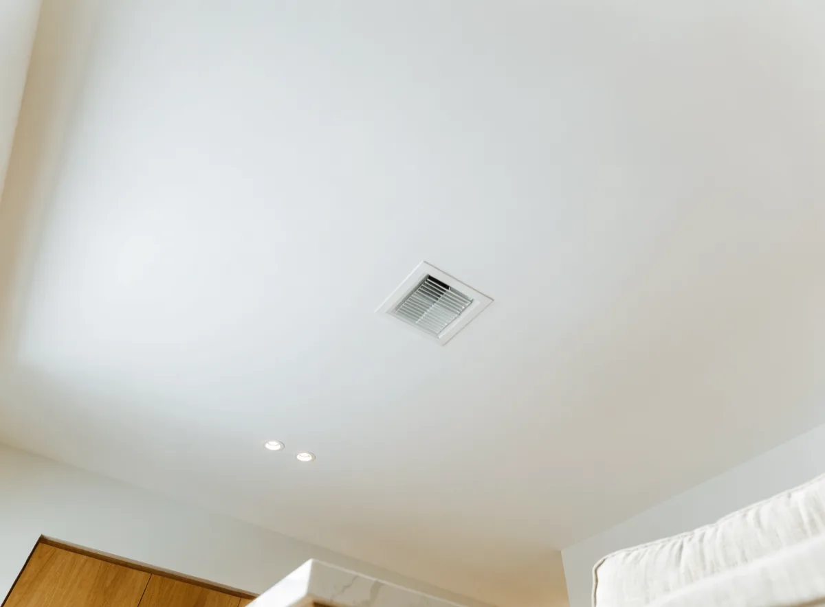 A flush ceiling supply diffuser in the new continuous ceiling between the living area and the kitchen of a Davie house