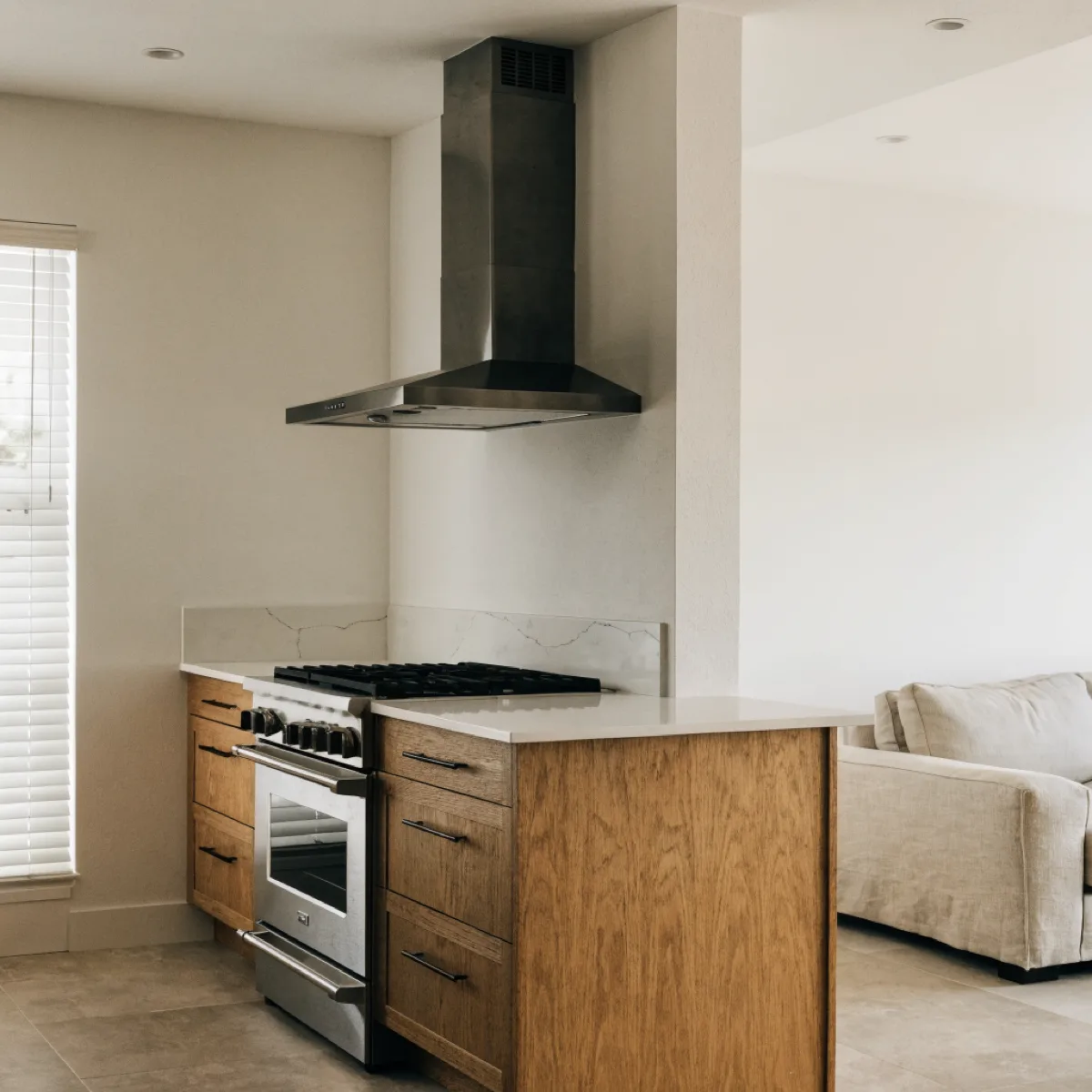A slim range hood ducted straight up into the ceiling over the range, with the living area of the same Davie room visible at the edge of the frame