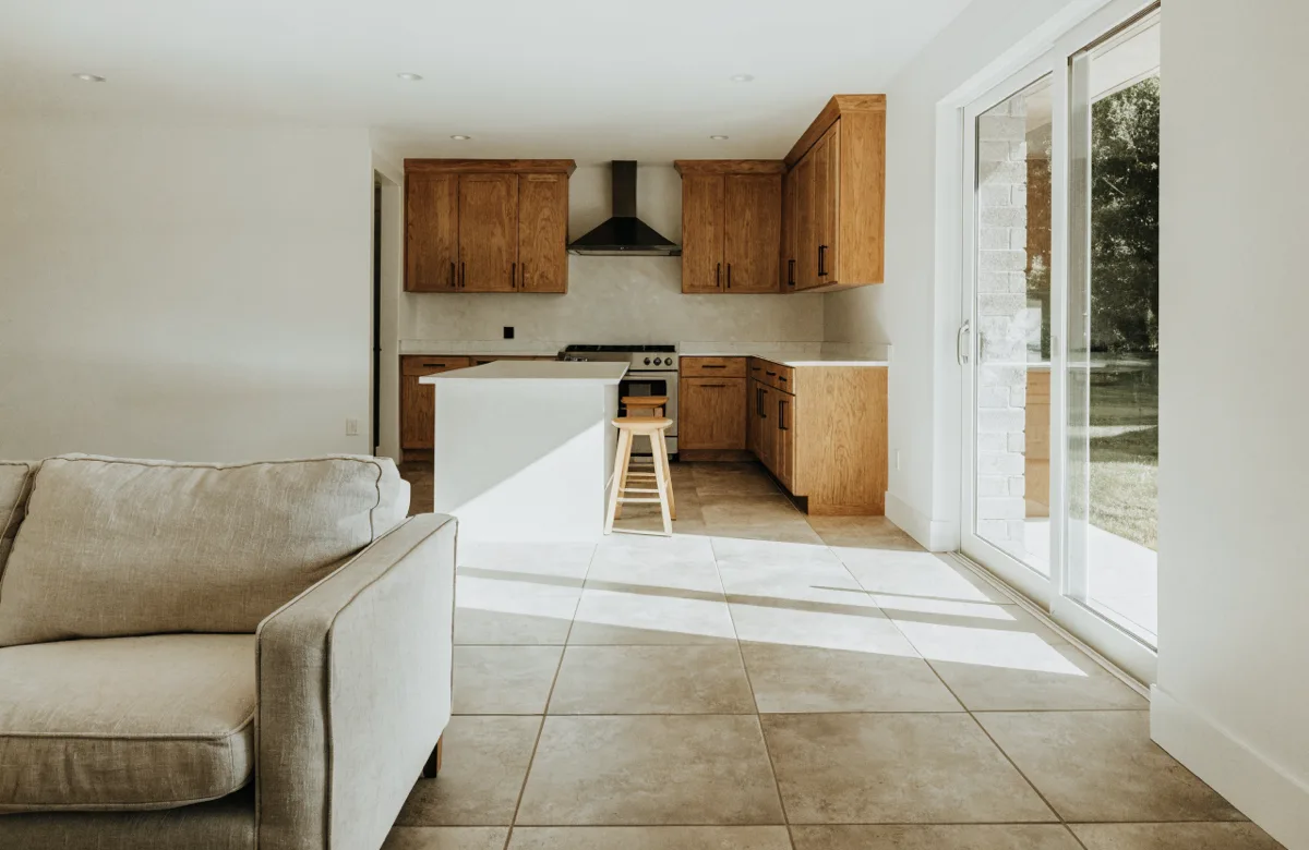 The same Davie room seen from behind the sofa, the back of the white island with its stools and the range wall beyond it, the floor tile running under both areas