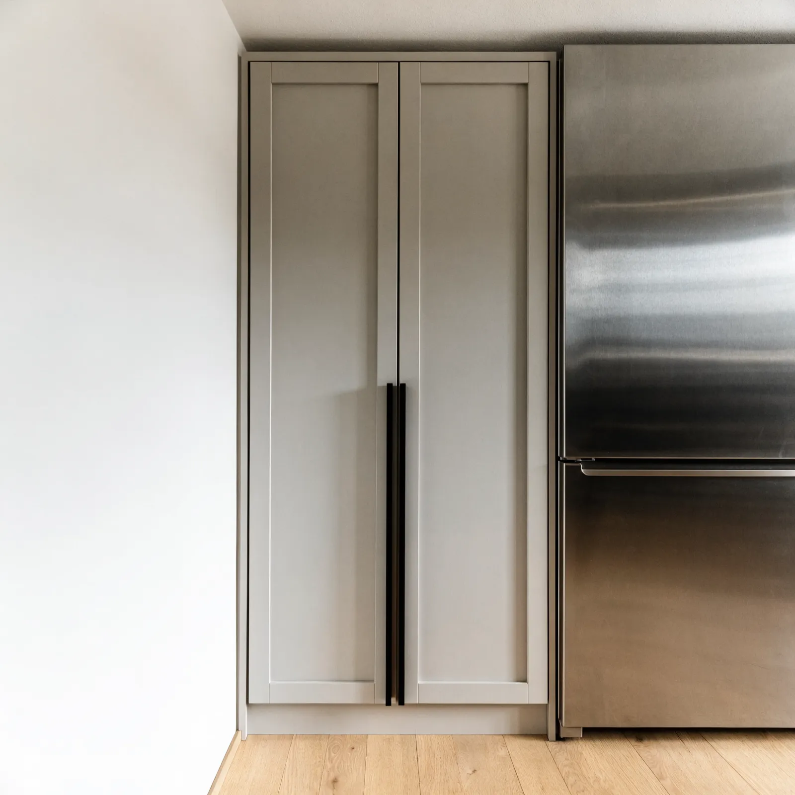 A single floor-to-ceiling pantry cabinet standing between a wall and the refrigerator, both doors closed, scribed tight to the ceiling