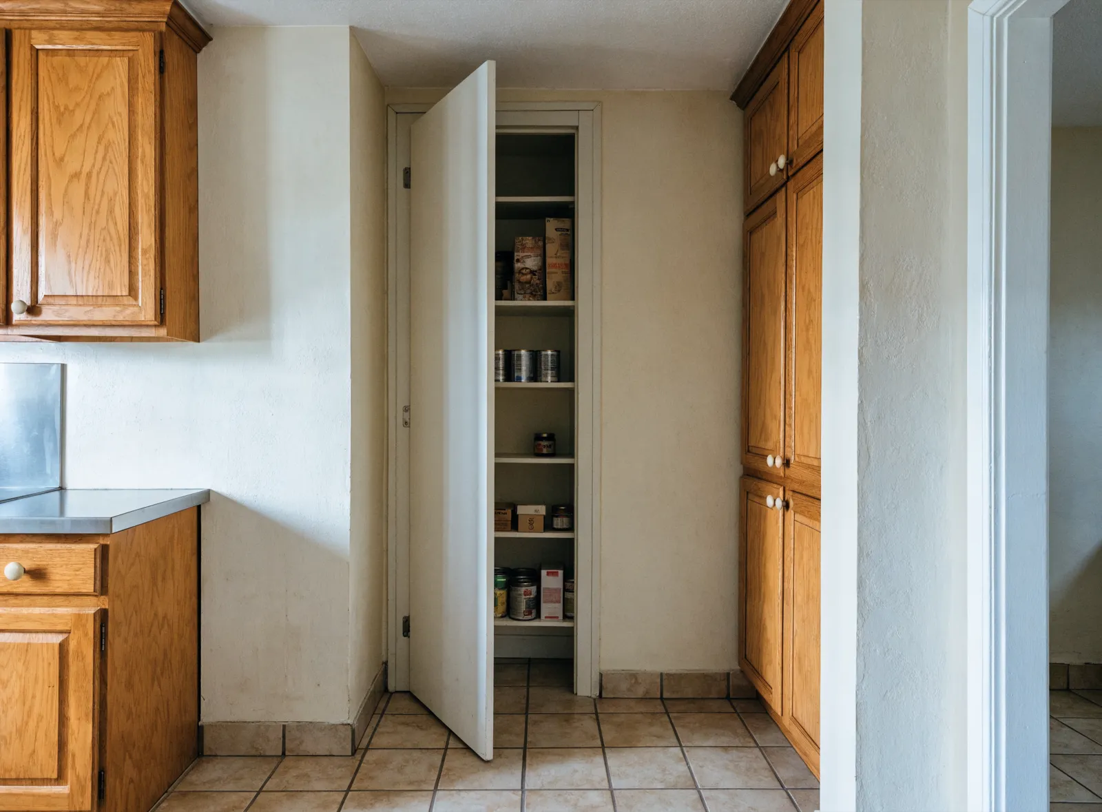 Pantry cabinets in Davie, FL: the original shallow pantry closet of an eighties house, its narrow door open on four fixed wood shelves packed one item deep