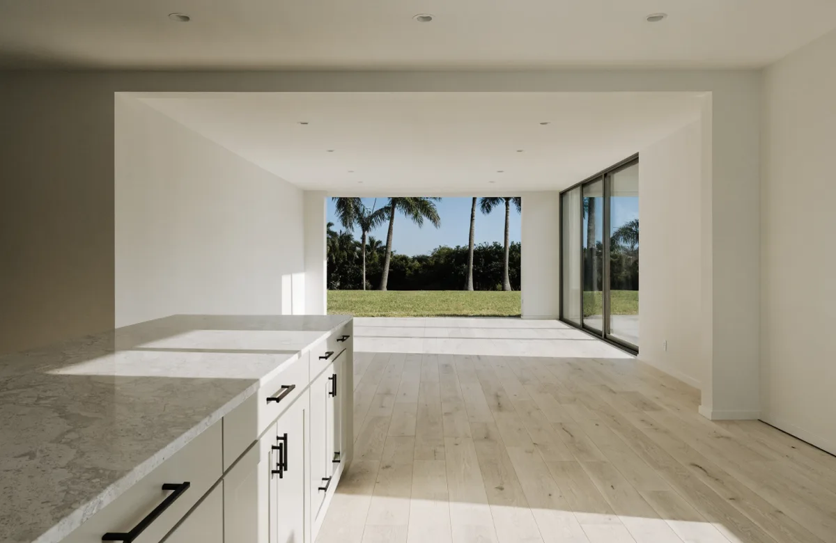 A wide opening between a Davie kitchen and its living room seen from the counter, the living room fully visible through it and the floor running through both rooms without a break